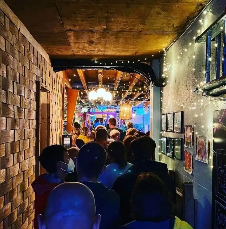 Crowded indoor venue with visitors walking through a narrow corridor decorated with string lights and brick walls.