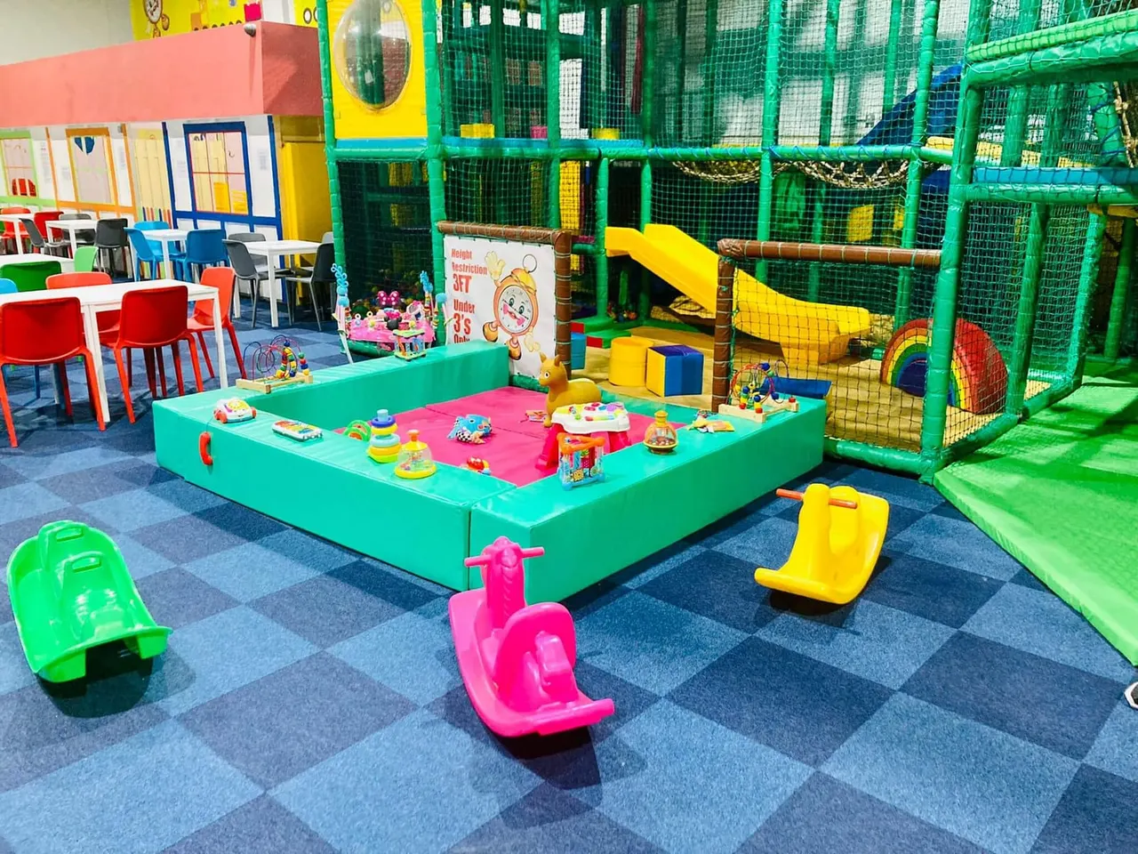 Colourful indoor play area with ball pit, climbing structures, toys and seating for young children.