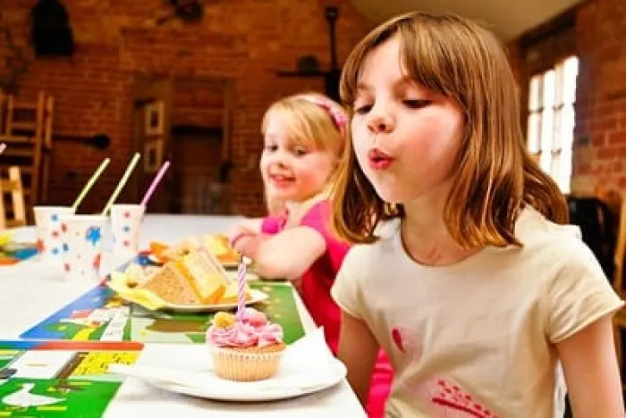 Two young children at a table blowing out candles on a birthday cupcake indoors.