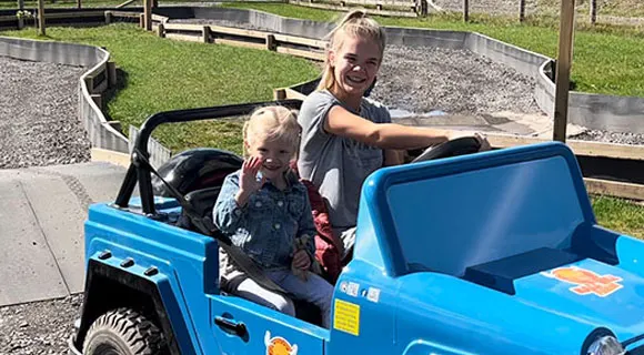 Two young children in a bright blue miniature electric vehicle at a farm attraction.