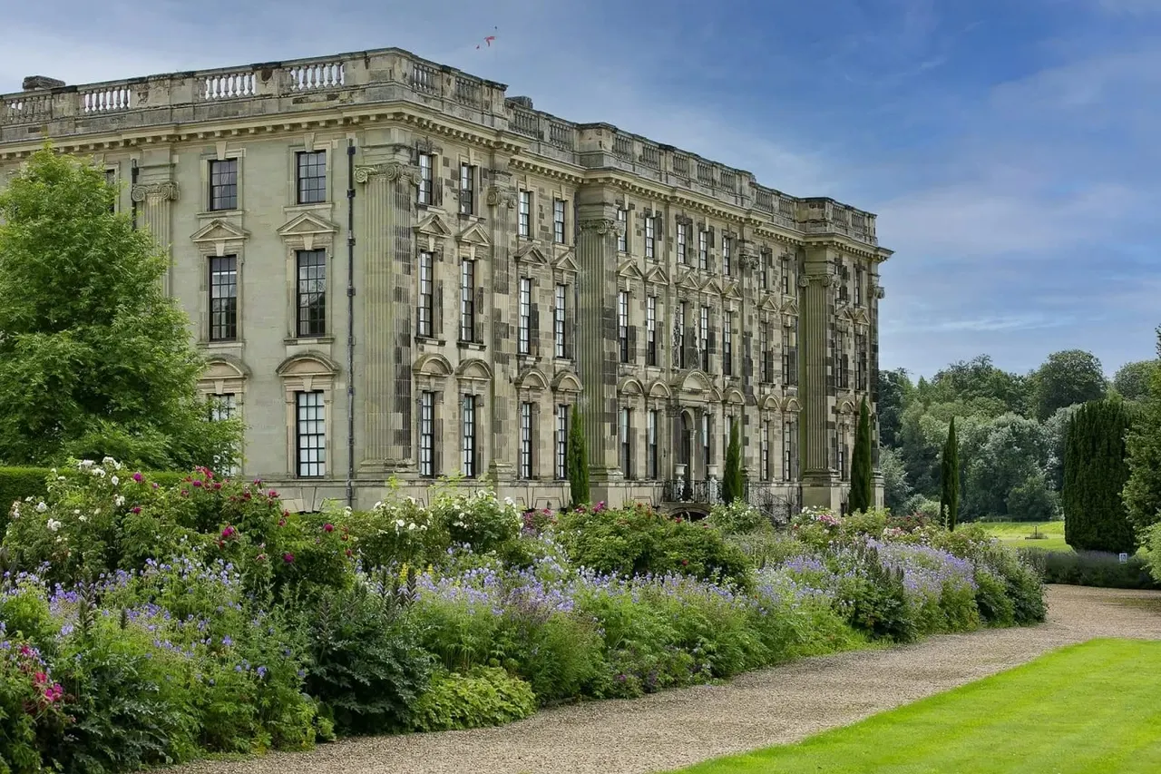 Grand stone mansion with classical architecture, formal gardens with flowering shrubs and lavender in foreground.