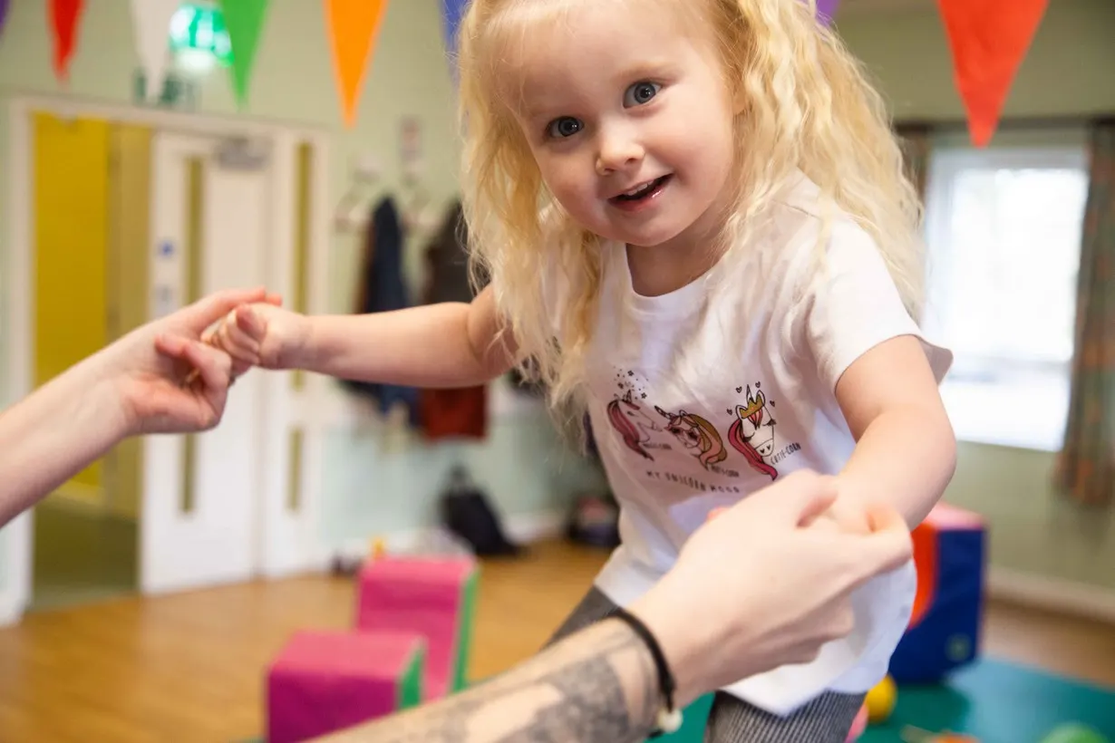 Young child playing with colourful building blocks in a decorated indoor play space with bunting.