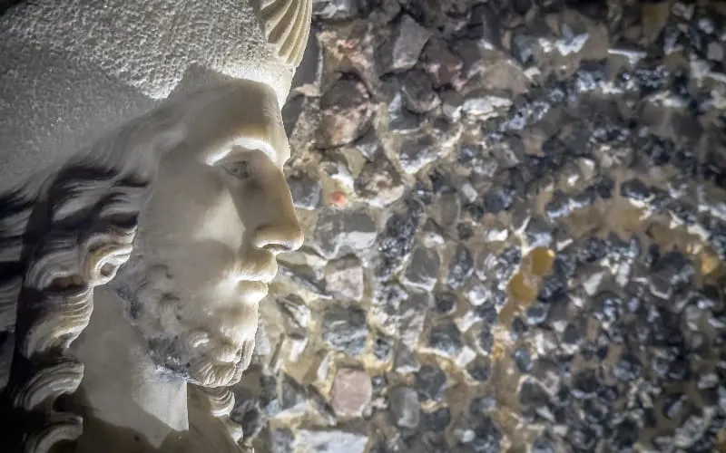 Close-up of a classical stone bust against a textured stone wall.