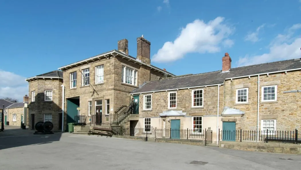 Stone-built historic buildings with multiple chimneys surrounding a paved courtyard under blue sky.