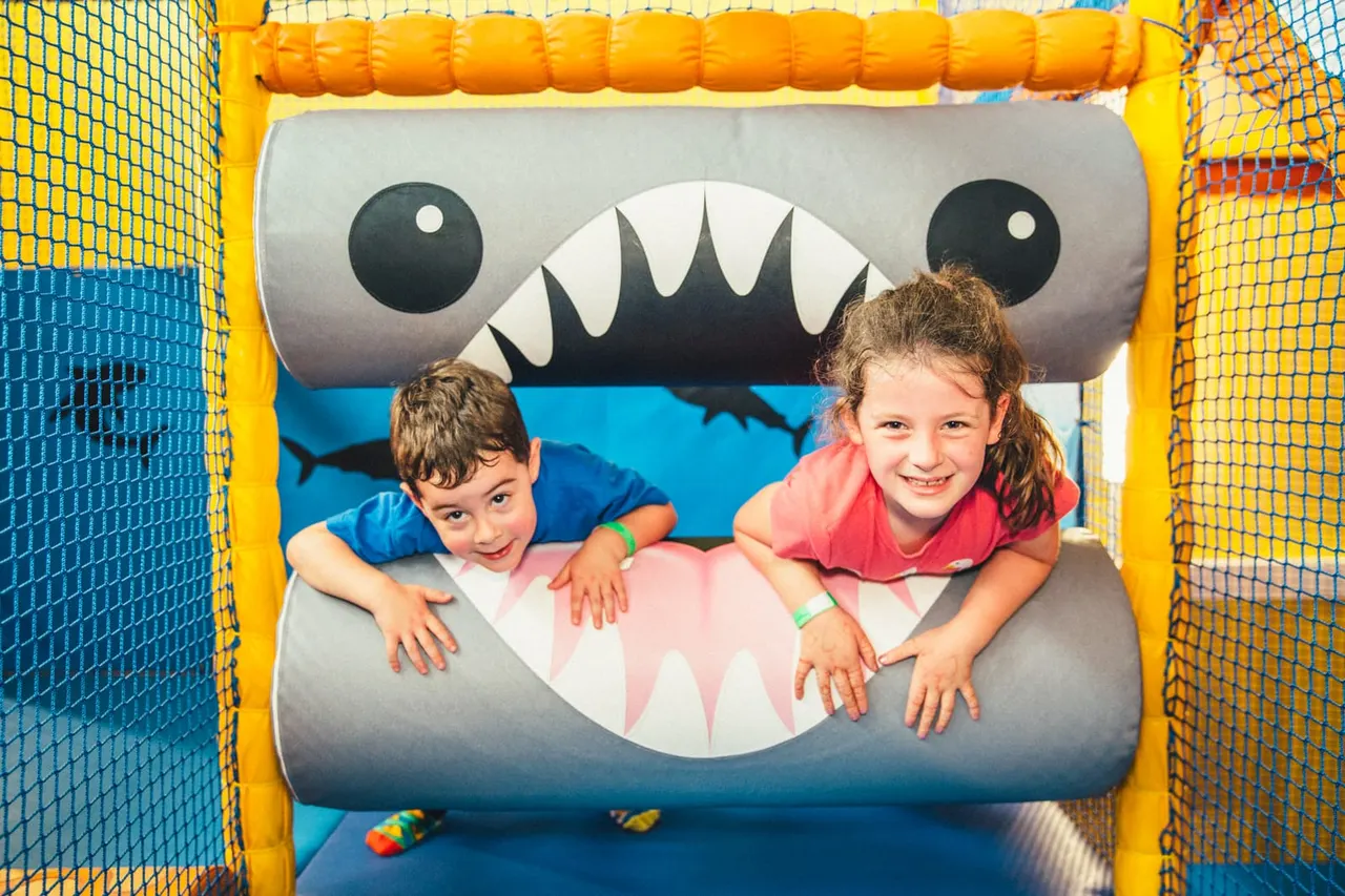 Two young children playing inside a monster-themed inflatable bounce house with googly eyes and teeth designs.