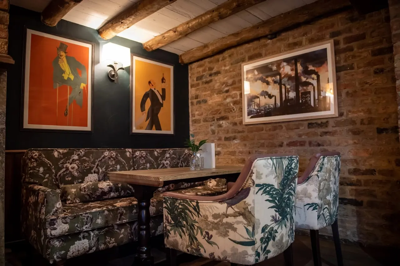 Interior seating area with vintage artwork, exposed brick walls, wooden beams, and patterned upholstered furniture.