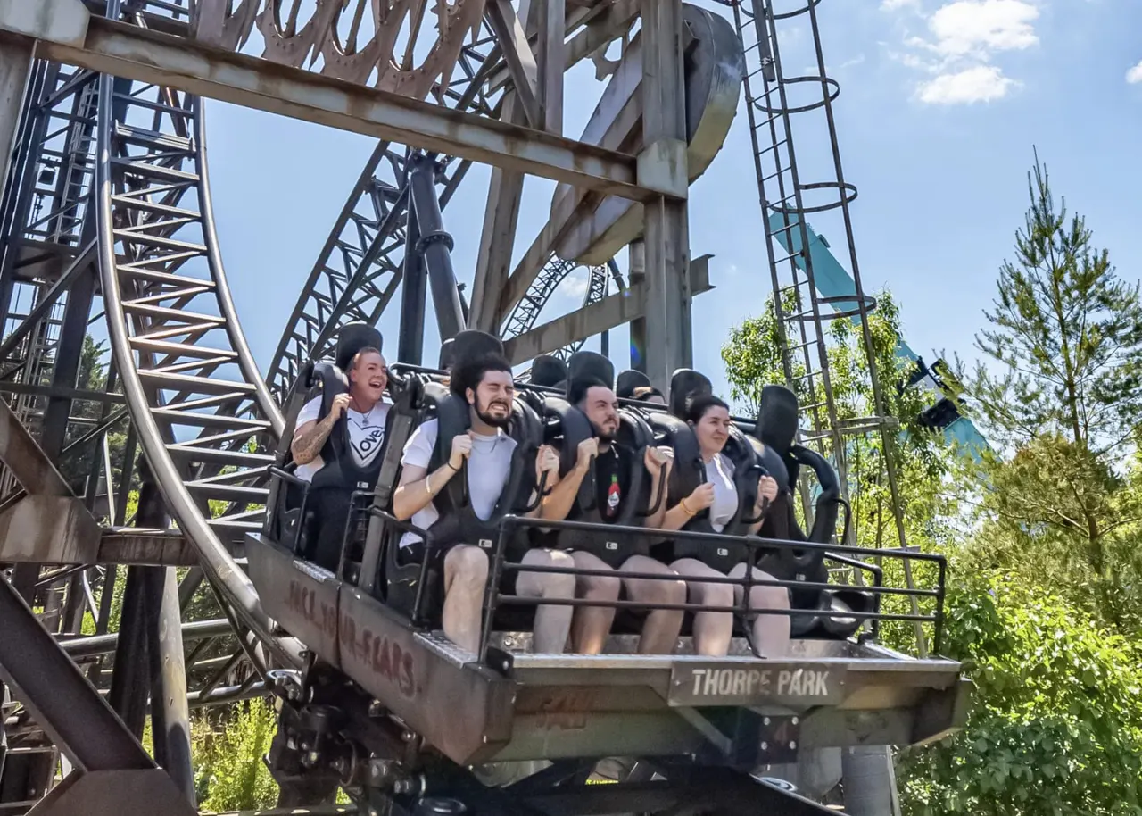 A group of six people enjoying a thrilling roller coaster ride with their hands raised, smiling amid the steel track structure.