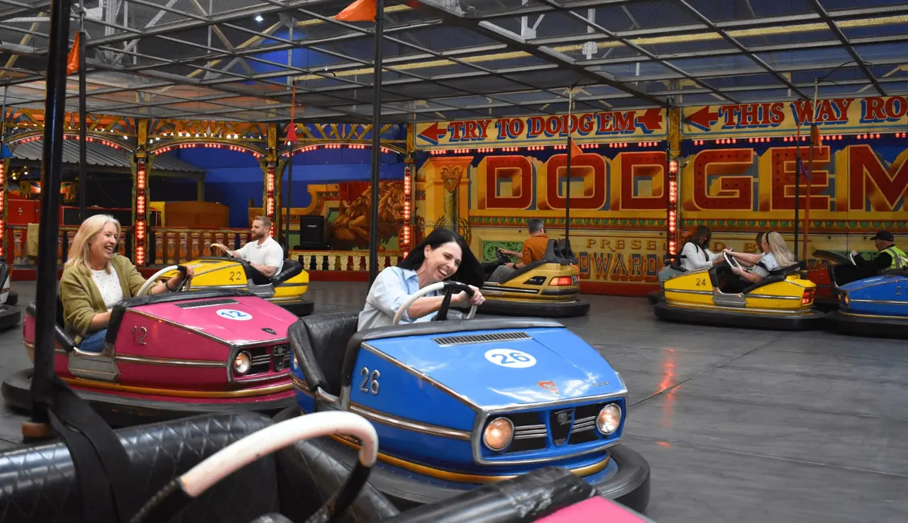 People operating colourful bumper cars at an indoor fairground ride with vintage-style decorated backdrops and signage.