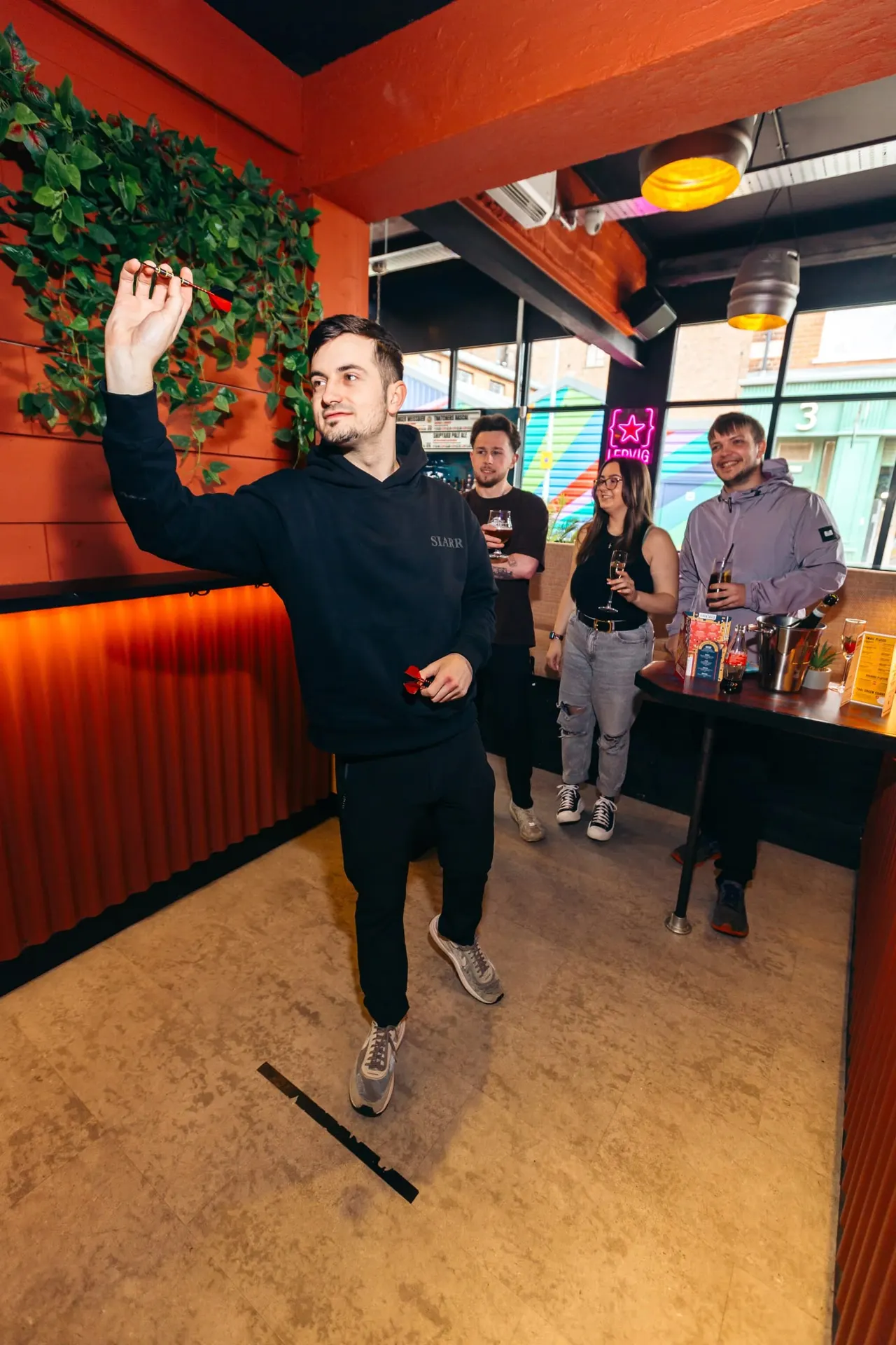 A man jumps with his fist raised whilst four others hold drinks in a vibrant red-walled bar interior.