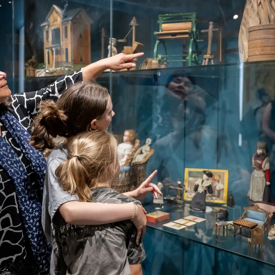 Two children pointing at a museum display case containing miniature historical models and figures.