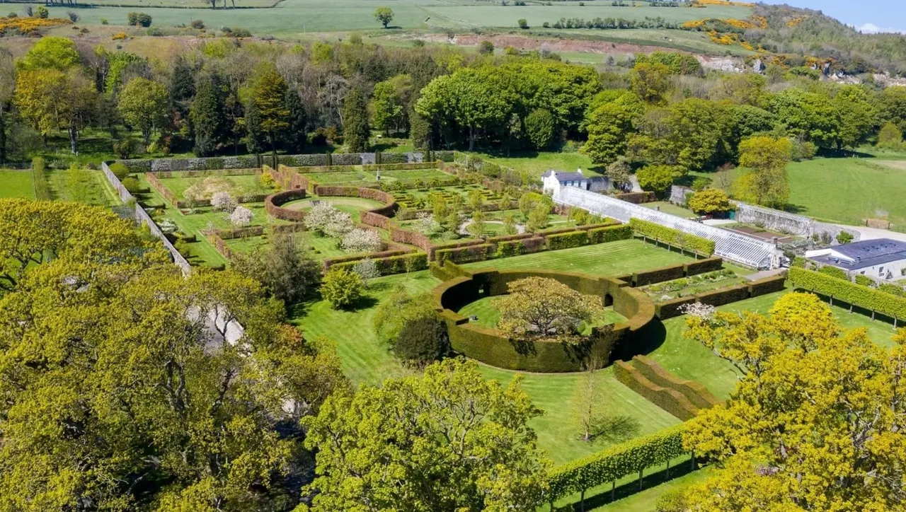 Aerial view of formal gardens with hedged parterre, circular sunken garden, and surrounding woodlands with rolling countryside beyond.