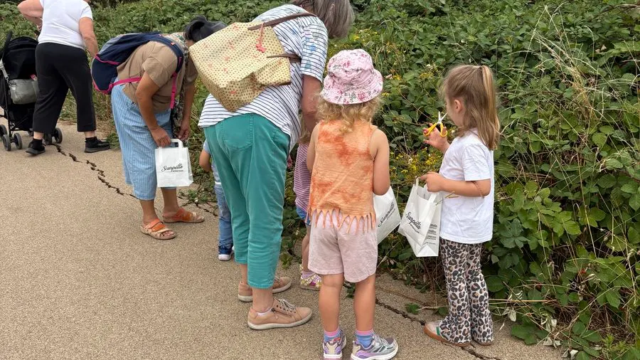 Adults and children gathered on a path beside overgrown vegetation during an outdoor activity session.