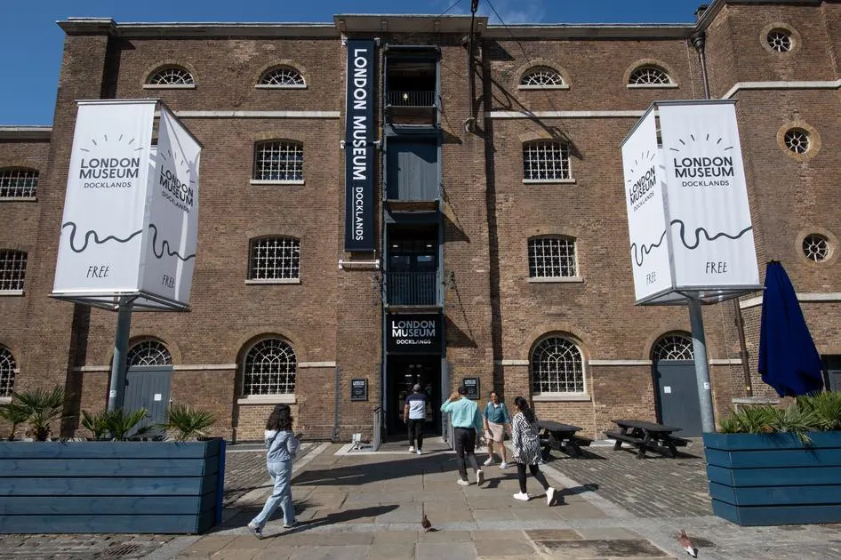 Visitors walking towards the entrance of a brick museum building with promotional banners on a sunny day.