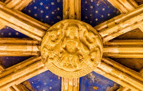 Ornate ceiling medallion with carved cherub surrounded by gilded wooden beams and blue starry panels.