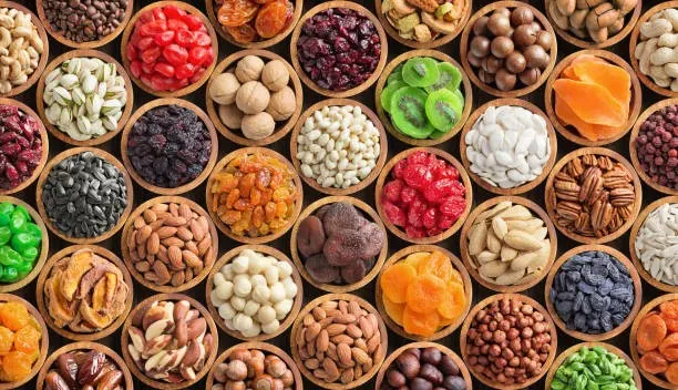 Overhead view of multiple wooden bowls filled with assorted nuts, dried fruits, and sweets.