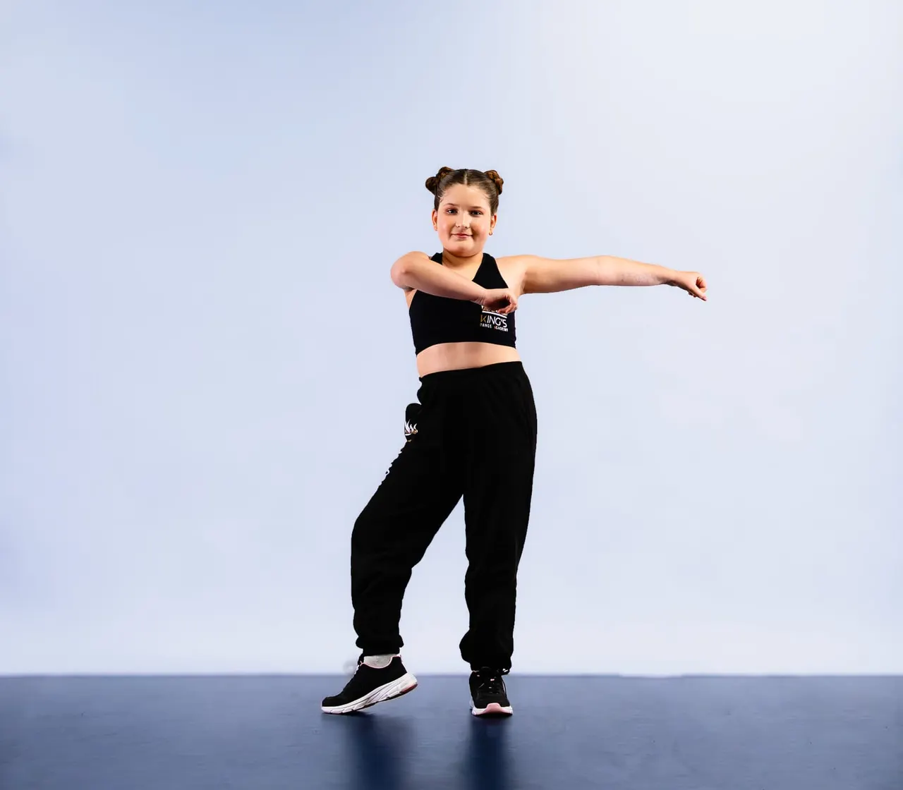 Young dancer in black sportswear striking a dynamic pose against a blue and grey background.
