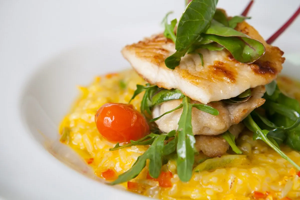 Seared fish fillet stacked on mushrooms and saffron risotto, garnished with pea shoots and red caviar.