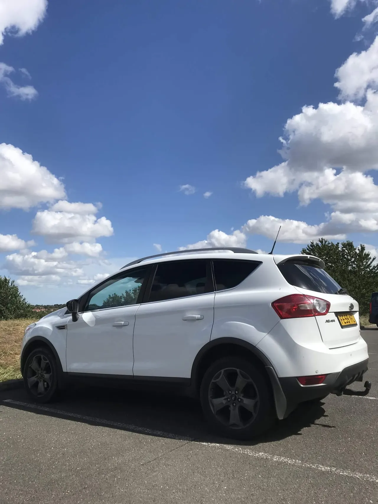 White SUV parked on tarmac with clear blue sky and white clouds in background.