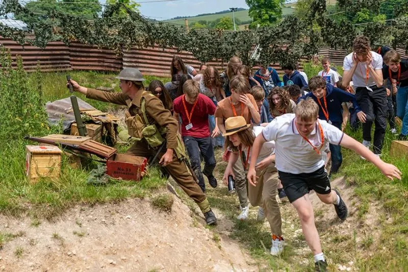 A group of children and adults participate in an interactive World War One trench activity at an outdoor historical festival.