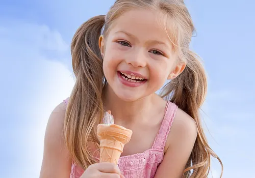 Young girl smiling whilst holding an ice cream cone against a blue sky.