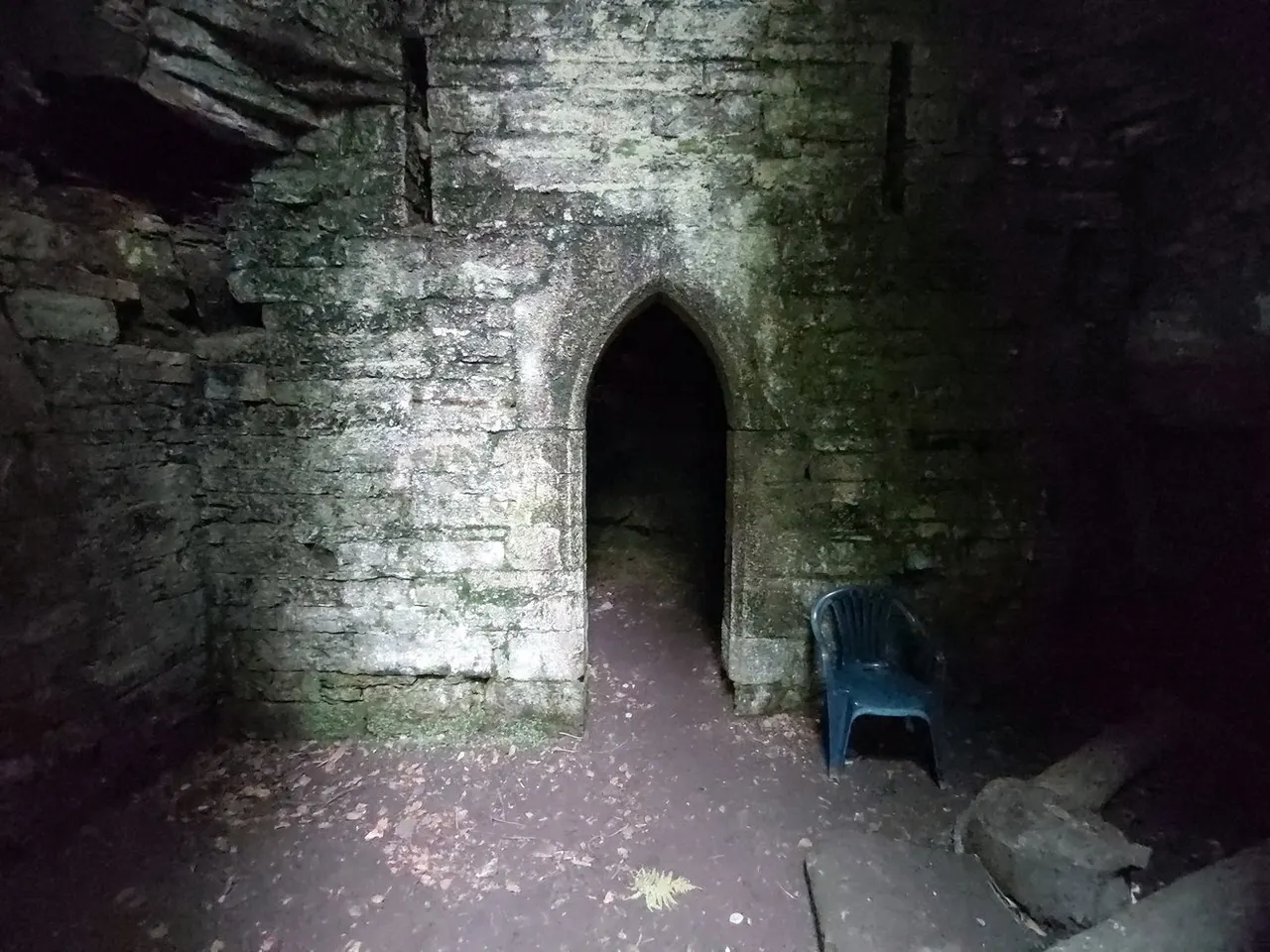Stone cave interior with Gothic-style arched doorway and blue plastic chair on the ground.