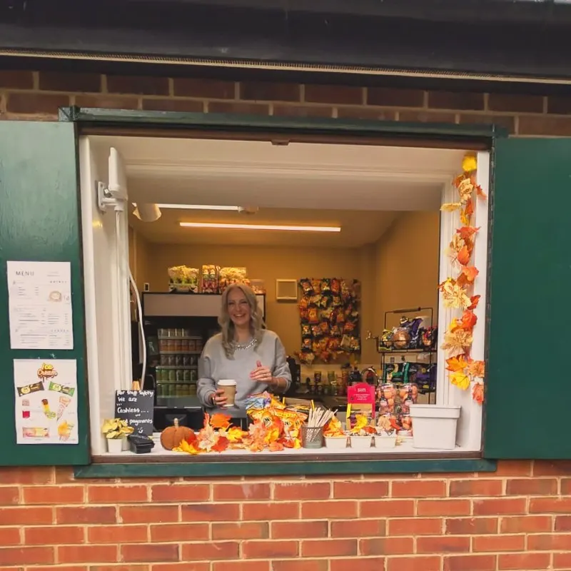 Woman serving at a small kiosk window decorated with autumn leaves and seasonal products.