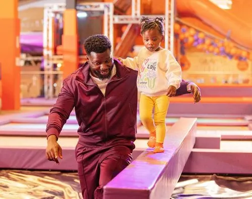 Adult and young child playing on an indoor soft play structure with purple and orange lighting.