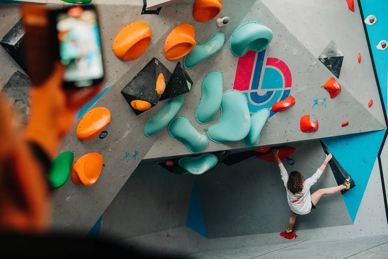 Child climbing an indoor rock wall with colourful hand and foot holds, photographed from above.