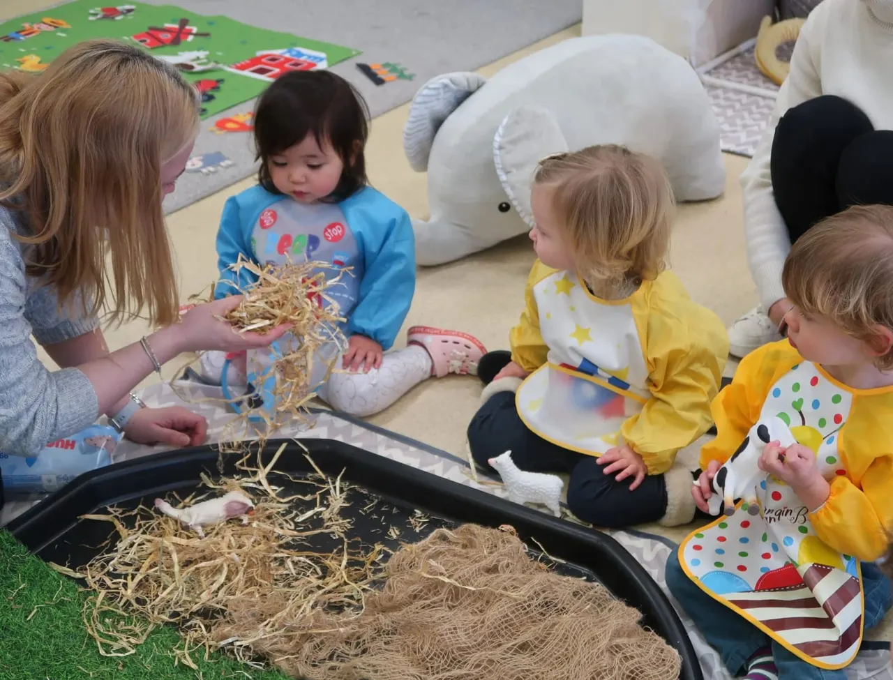 Young children playing with straw in a sensory bin during an indoor activity session.