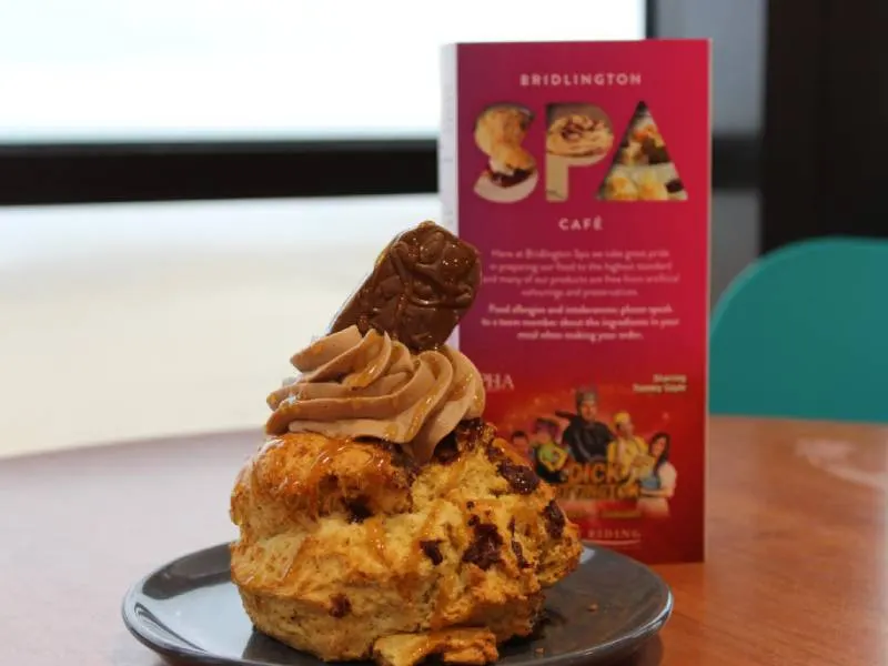 A decorated scone with cream and chocolate topping on a black plate, with a Bridlington Spa Café menu card behind it.