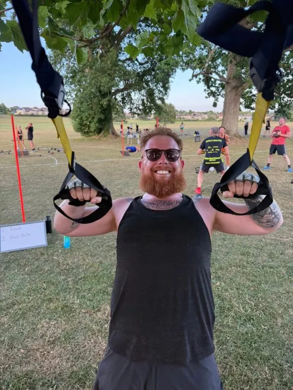 Man doing suspension training with straps during outdoor fitness class in a park.