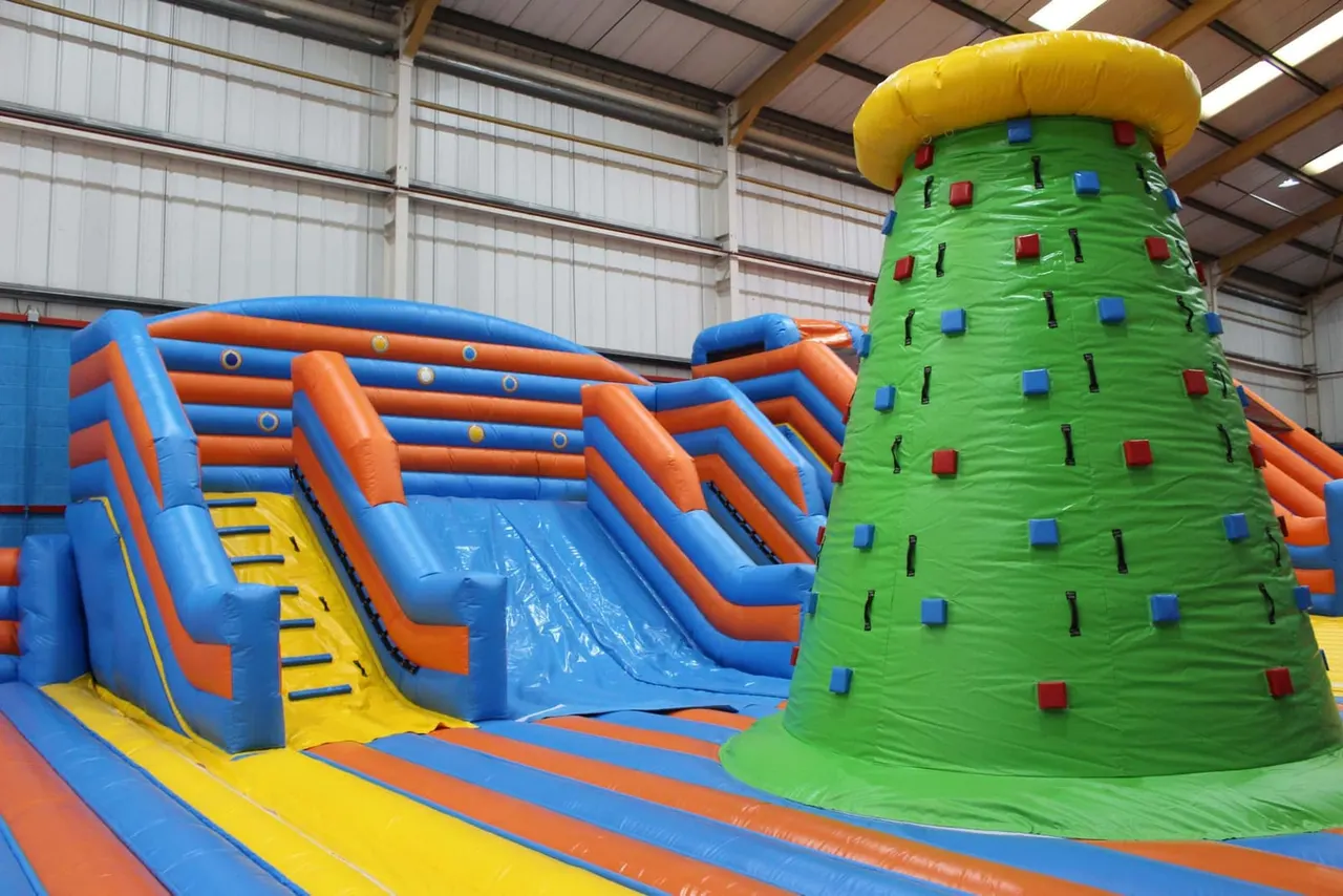 Colourful inflatable play equipment including a climbing tower and slide inside an indoor leisure facility.