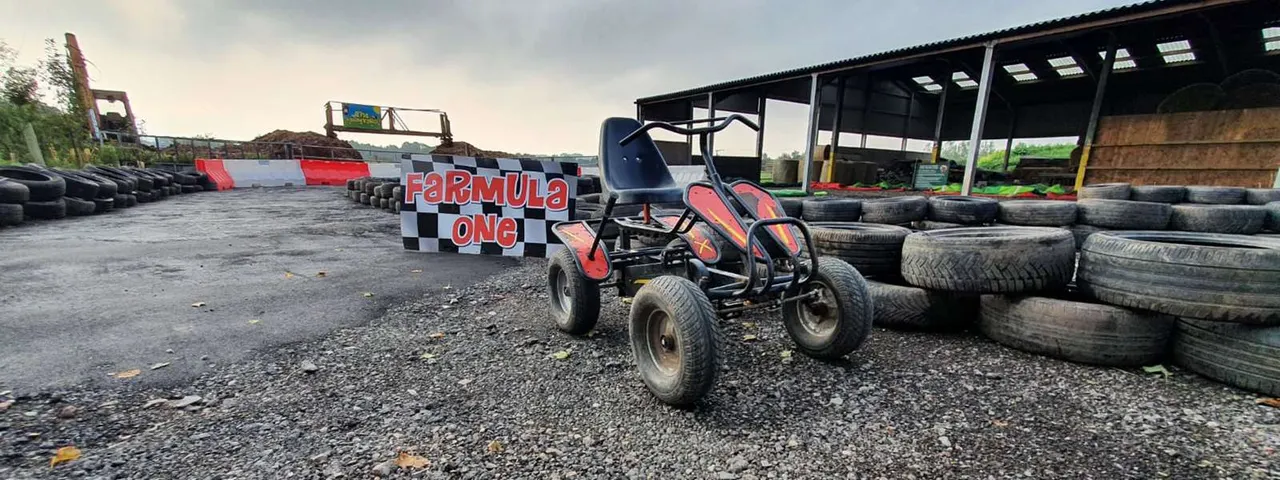 Red and black go-kart on a gravel track surrounded by tyres and Formula One signage at an outdoor racing venue.
