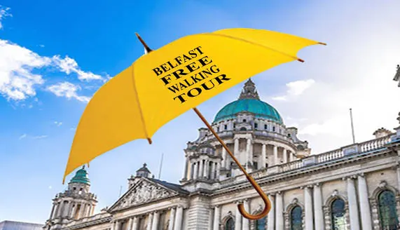 A yellow umbrella branded with "Belfast Free Walking Tour" held up in front of a grand neoclassical building with a domed roof under blue sky.
