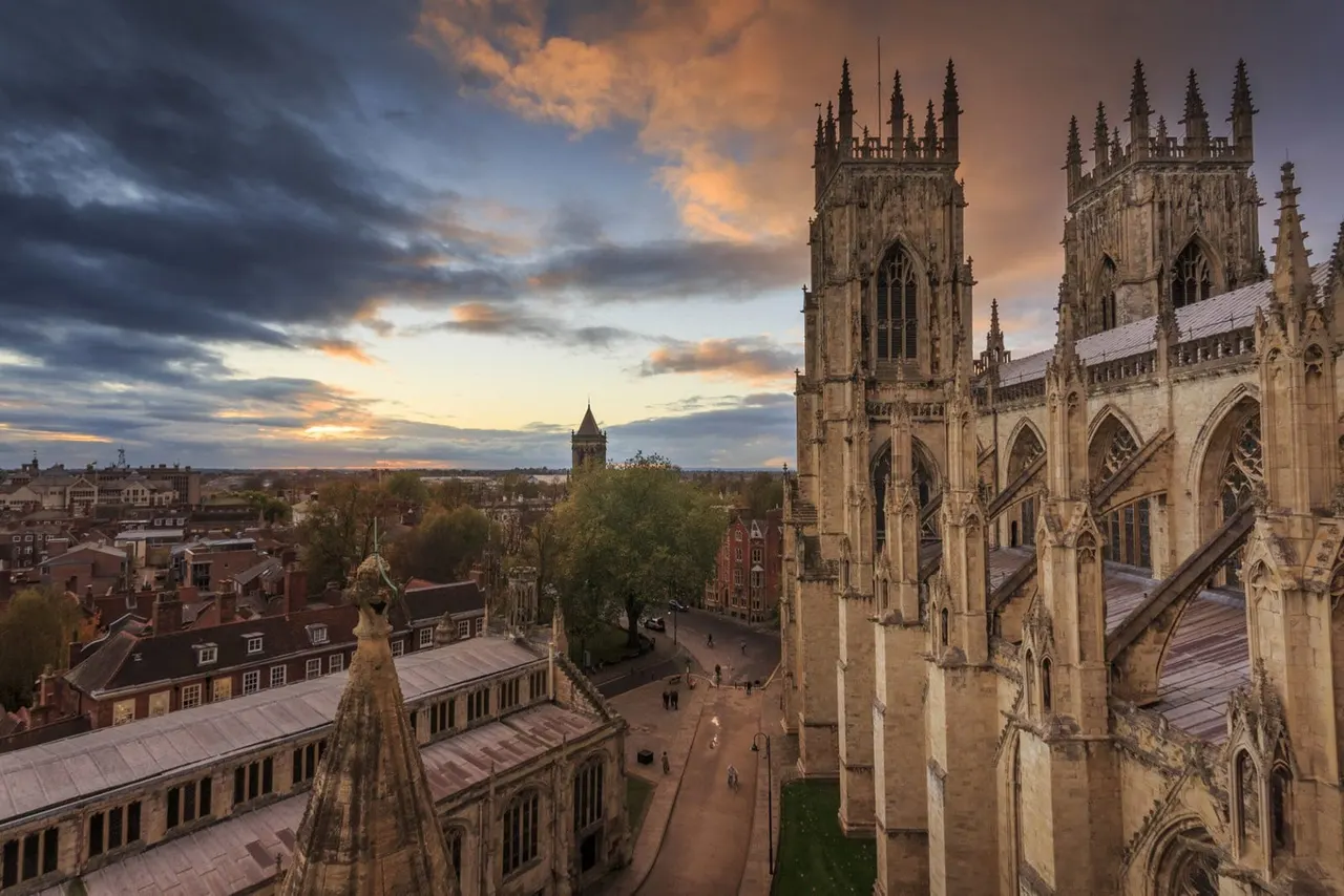 Gothic cathedral with twin towers at sunset, overlooking a medieval city square and surrounding rooftops during golden hour.