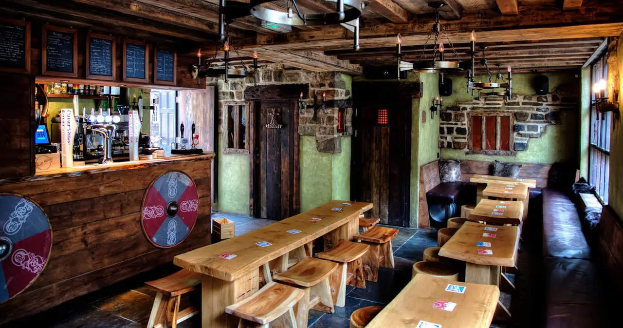Interior of a Viking-themed pub with wooden tables, benches, a bar counter, exposed beams and stone walls painted green.