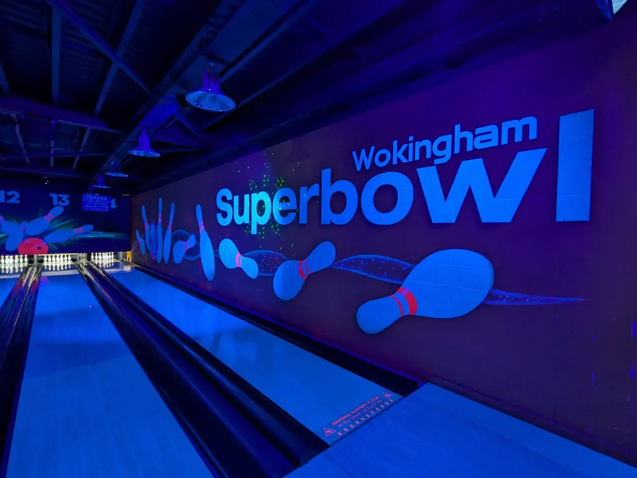 Illuminated bowling lanes with blue neon lighting and signage at an indoor bowling alley.