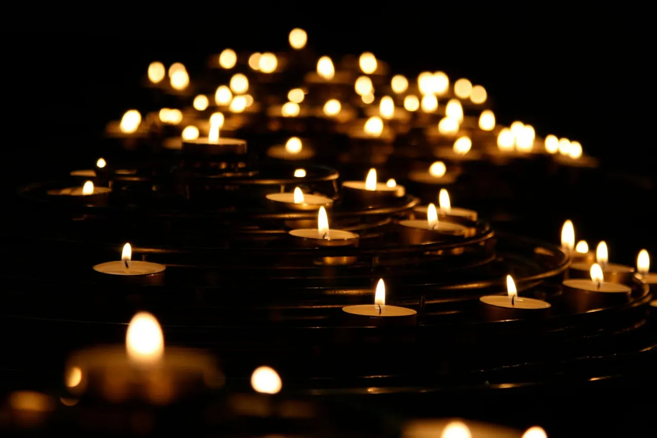 Multiple lit tea lights arranged in a circular pattern against a dark background.