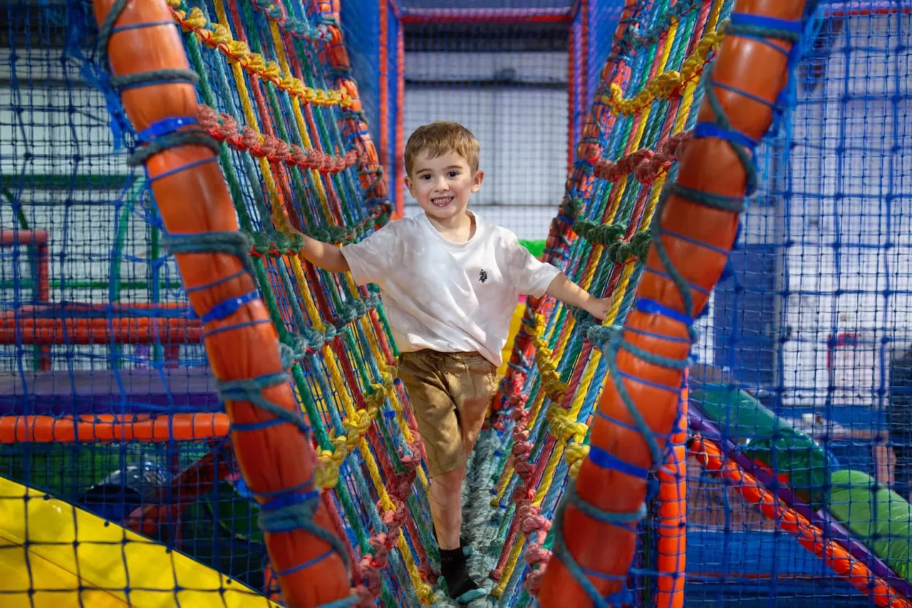 Young child playing inside a colourful soft play structure with orange tubes and mesh netting.