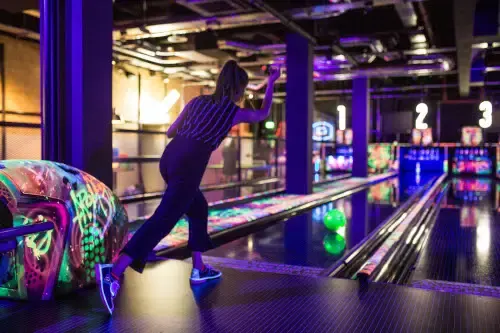 Person bowling at night with neon-lit lanes and colourful illuminated ball returns.