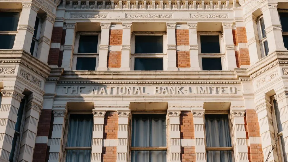 Historic Victorian building facade with ornate stone columns and red brick detailing, showing "The National Bank Limited" signage.