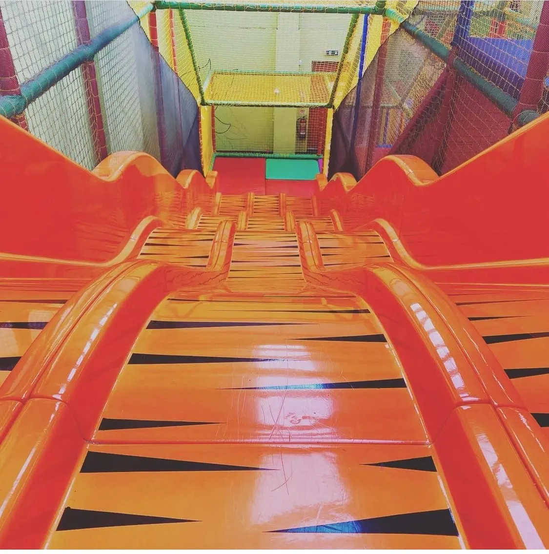 Interior view down a red and orange inflatable slide with netting and colourful play structures visible at the top.