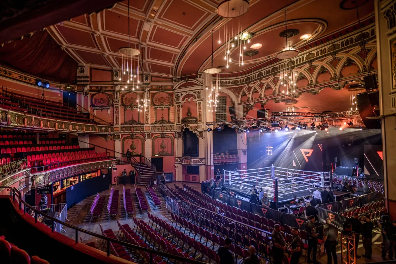 Historic theatre with ornate red and gold interior hosting a boxing match in the ring, with spectators seated in multiple tiers.