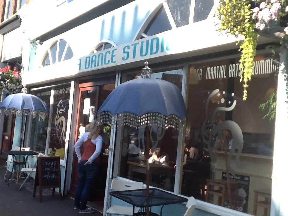 People sheltering under umbrellas outside a dance studio storefront on a rainy street.