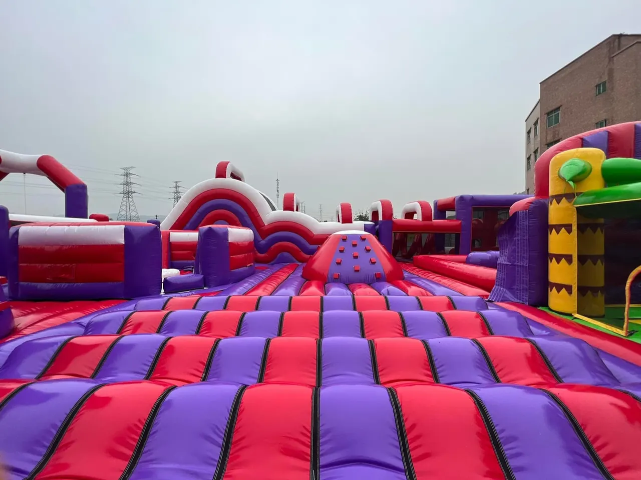 Outdoor inflatable bounce park with various red and purple padded play structures, slides, and obstacles.
