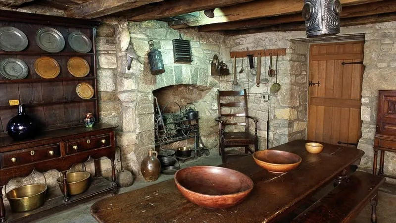Historic kitchen interior with wooden table, traditional cooking hearth and period furnishings and utensils.