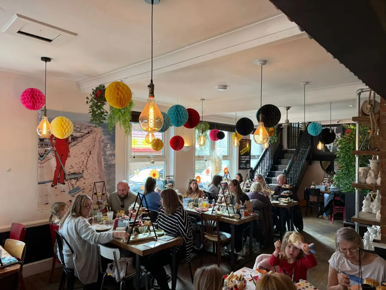 Colourful decorated café interior with diners seated at tables beneath hanging paper lanterns and pendant lights.