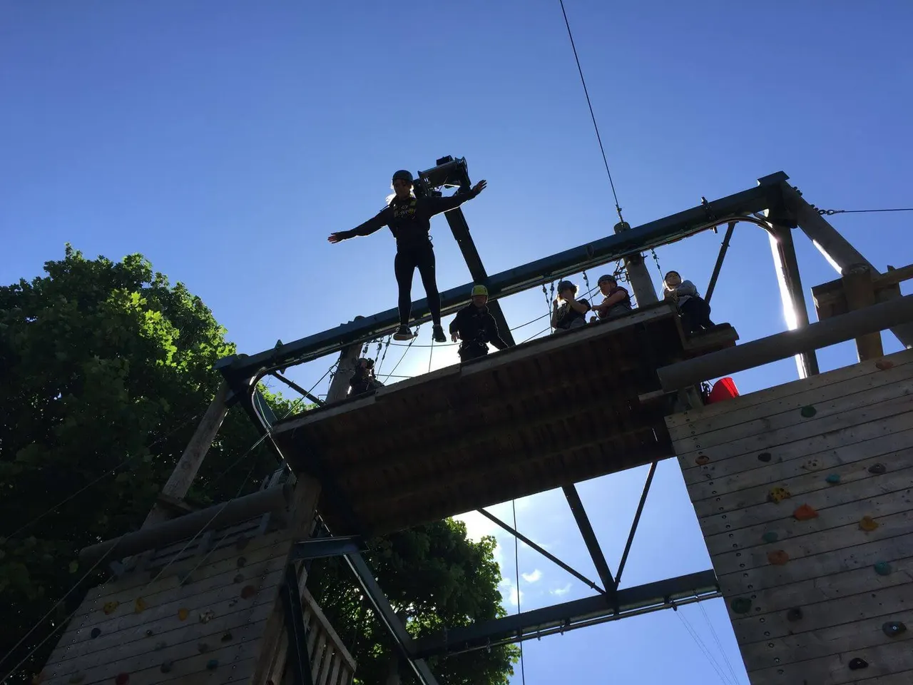 Person on high ropes course balancing on beam whilst others watch from platform below.