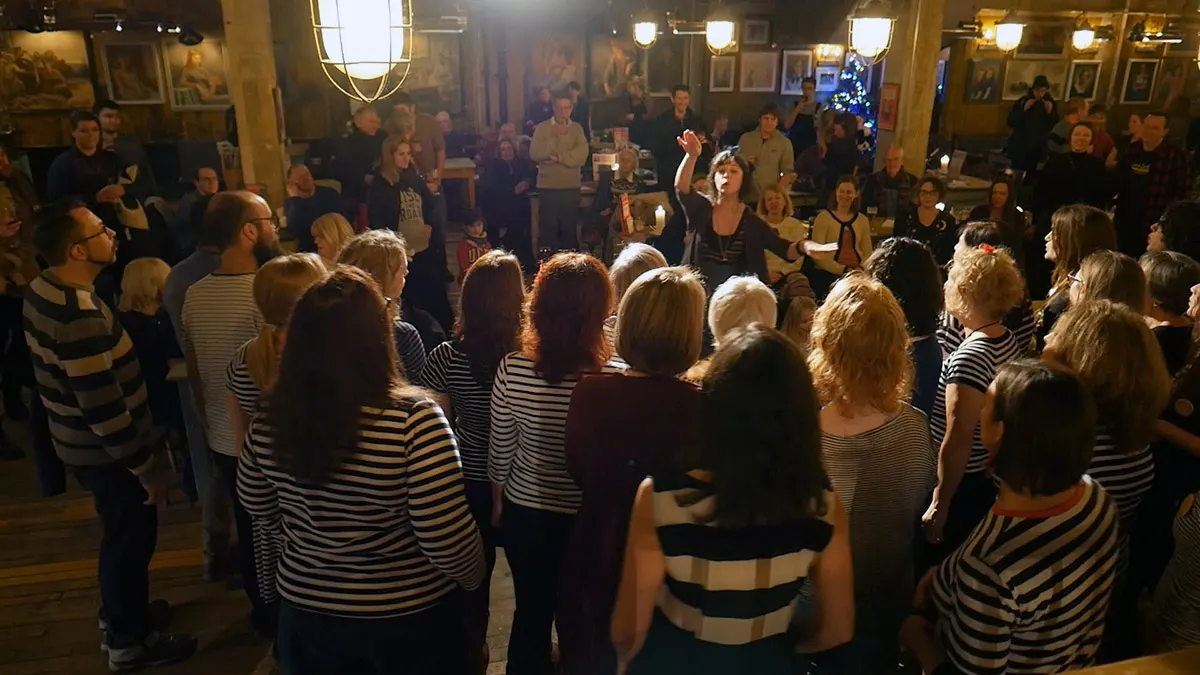 Large group of people wearing striped tops dancing together in a decorated indoor venue at night.