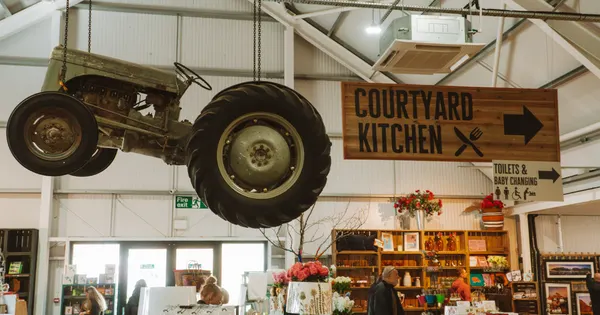 Vintage tractor suspended from ceiling above farm shop interior with signage and retail displays below.
